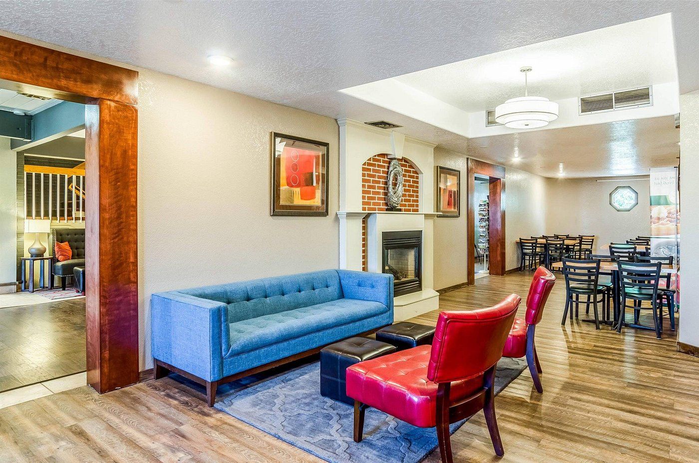 A modern living room with a blue sofa, red chairs, a fireplace, and a dining area with tables and chairs.