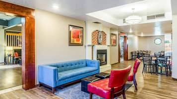 A modern living room with a blue sofa, red chairs, a fireplace, and a dining area with tables and chairs.