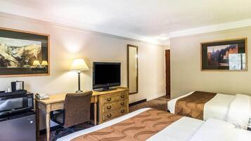 A hotel room with a desk, television, two beds, a chair, and a refrigerator.