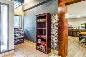 Una zona de recepción con pared de ladrillo, una estantería de madera con diversos objetos y un tablón de anuncios con postales.