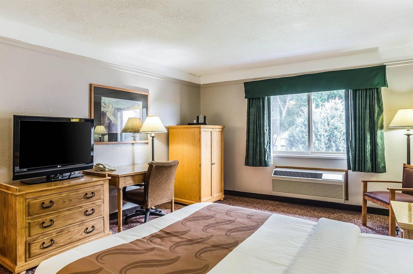 A hotel room with a bed, a desk with a television, a chair, a wardrobe, and a window with curtains.