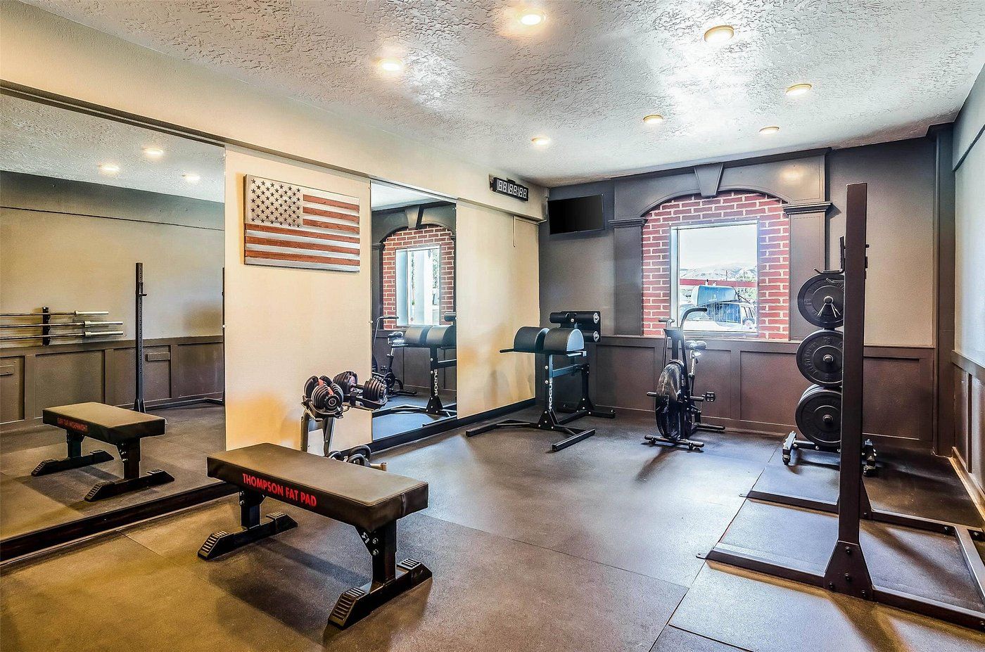 A gym with weightlifting equipment, a bench, and a mirror reflecting the American flag.