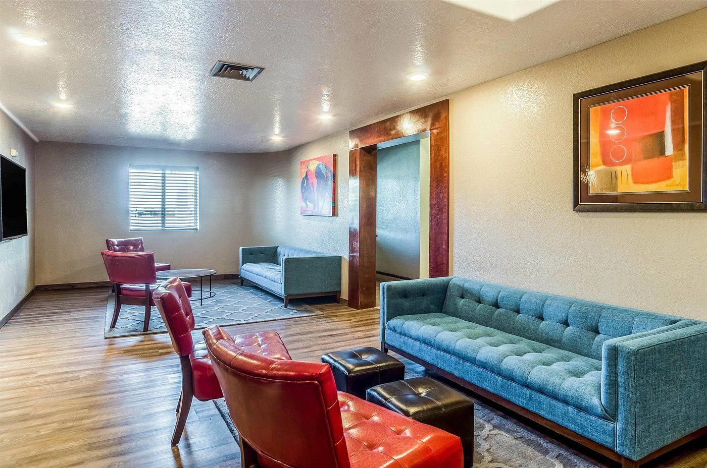 A room with a blue sofa, red chairs, a small table, and a framed artwork on the wall.