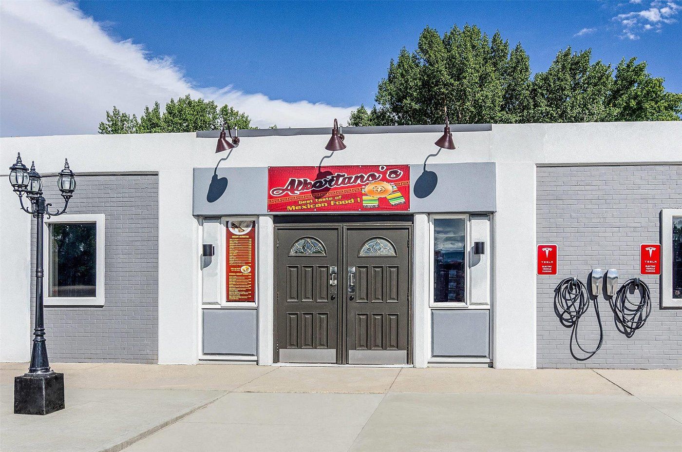A building with a sign for 'Alberto's Mexican Food' and two Tesla electric vehicle charging stations.