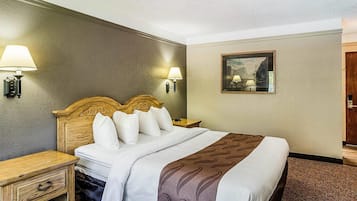 A hotel room with a bed, bedside tables, lamps, and a framed picture on the wall.