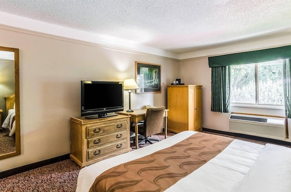 A hotel room with a bed, a desk with a chair, a television, a wardrobe, and a window with curtains.