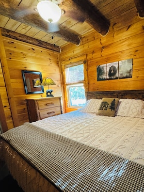 A wooden cabin room with a bed, a dresser, a lamp, and a window. - 3 mile scenic ride to WPG trails from Sunset Vista (Mena)