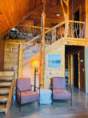 A wooden interior with a staircase, two chairs, a lamp, and a painting. - 3 mile scenic ride to WPG trails from Sunset Vista (Mena)