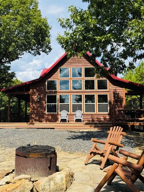 A wooden cabin with a red roof, large windows, and two Adirondack chairs on the porch. - 3 mile scenic ride to WPG trails from Sunset Vista (Mena)
