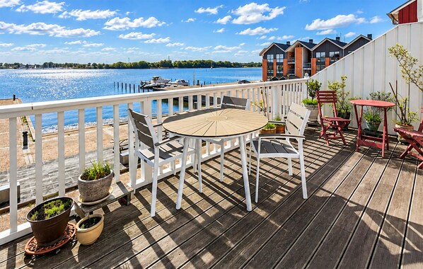 Een houten terras met een ronde tafel en stoelen, met uitzicht op een wateroppervlak met boten.