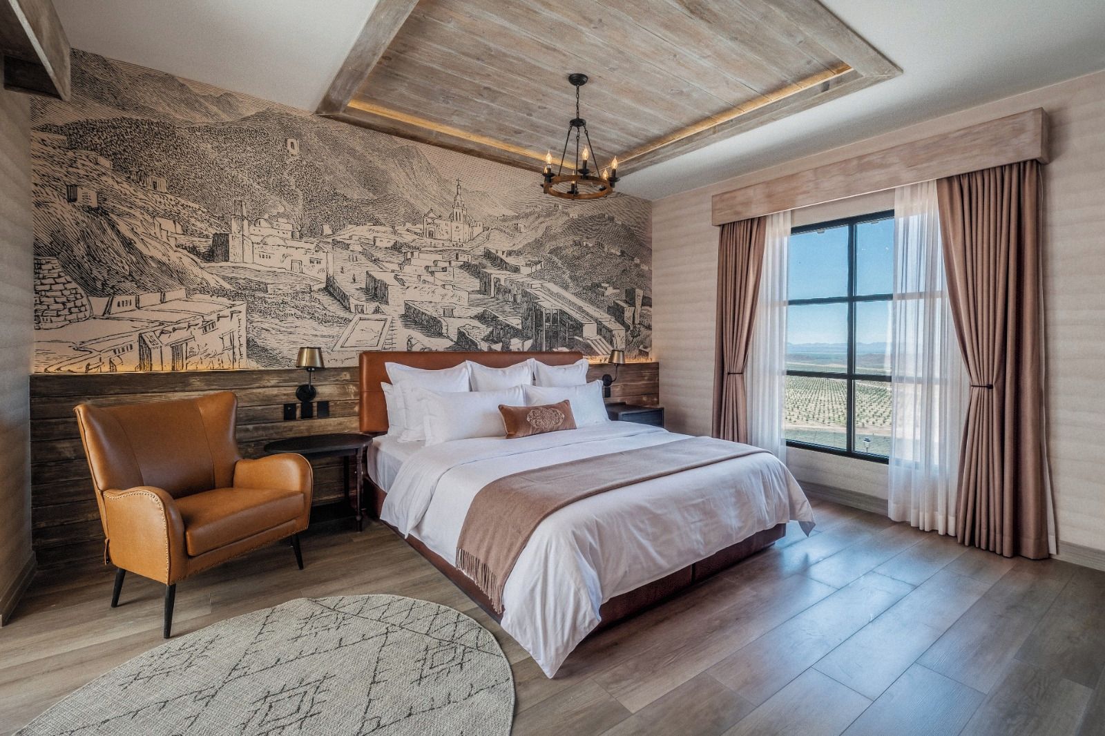 Un dormitorio con una cama grande, una silla, una mesita de noche, una lámpara y un mural en la pared.
