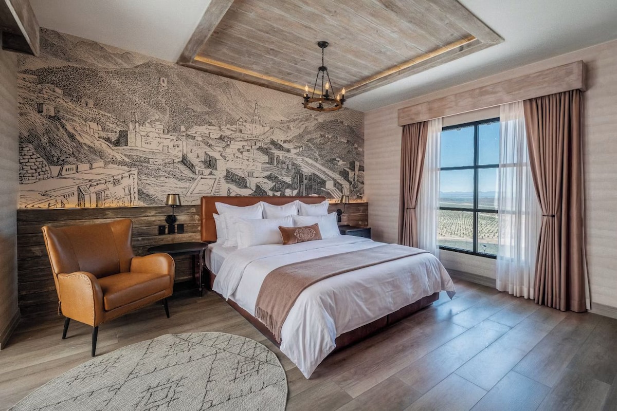 A bedroom with a large bed, a chair, a nightstand, and a wall mural.