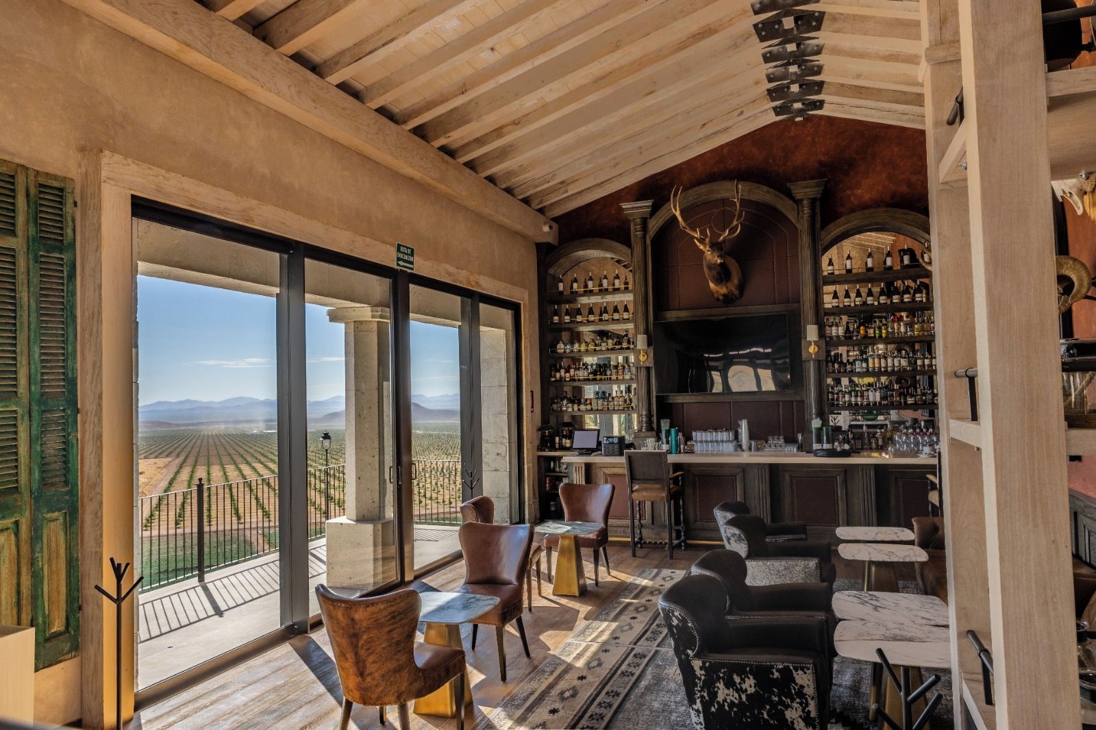 A bar area with a view of a vineyard, wooden ceiling, and a variety of seating options.
