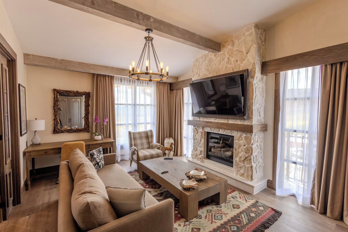A spacious living room with a stone fireplace, a large flat-screen TV, a chandelier, and a comfortable seating area.