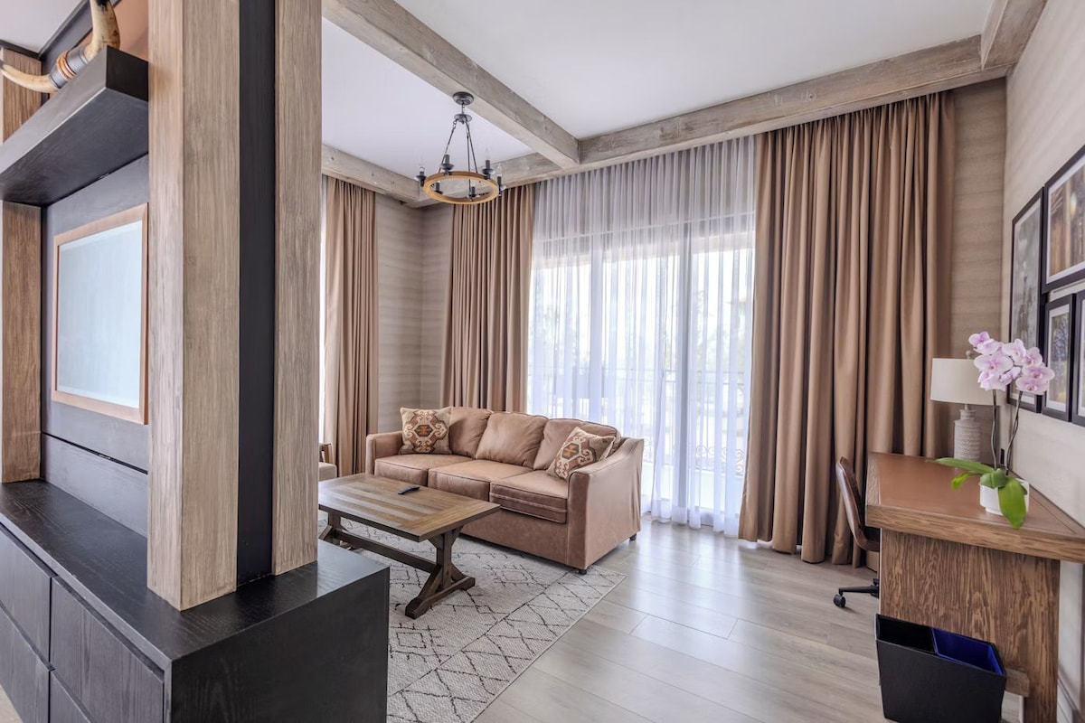 A modern living room with a sofa, coffee table, and a desk with a lamp and orchid plant.