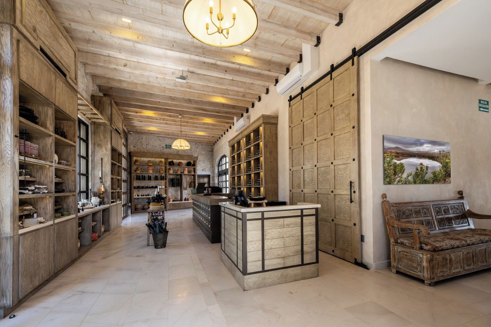 A spacious hotel lobby with wooden shelving, a reception desk, and a large window with a view of a lake.