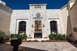Un edificio con fachada de piedra, una entrada central con puerta de madera y dos ventanas de arco a cada lado.