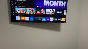 Een flatscreen televisie aan de muur, waarop een streamingdienst met diverse contentopties wordt getoond.