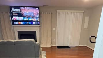 A living room with a flat-screen TV mounted above a fireplace, a gray sofa, and a wooden floor.