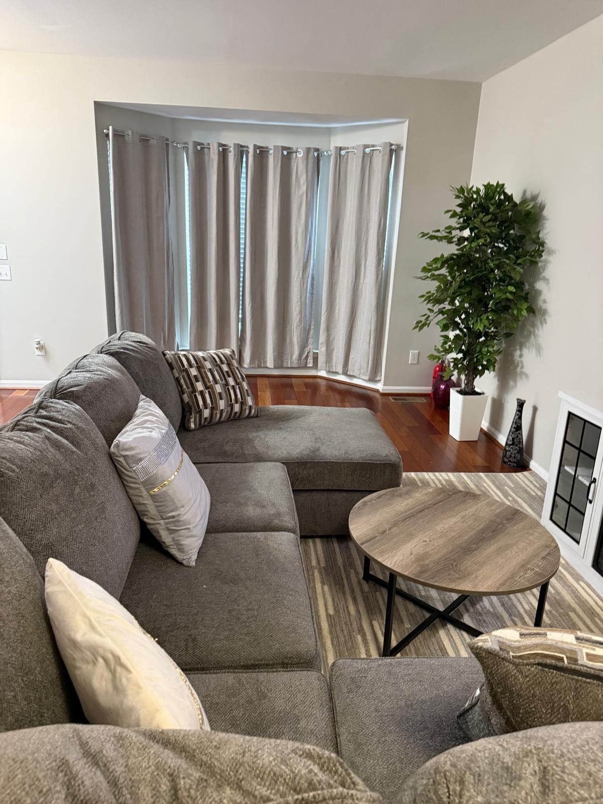 A living room with a sectional sofa, a round coffee table, and a potted plant.
