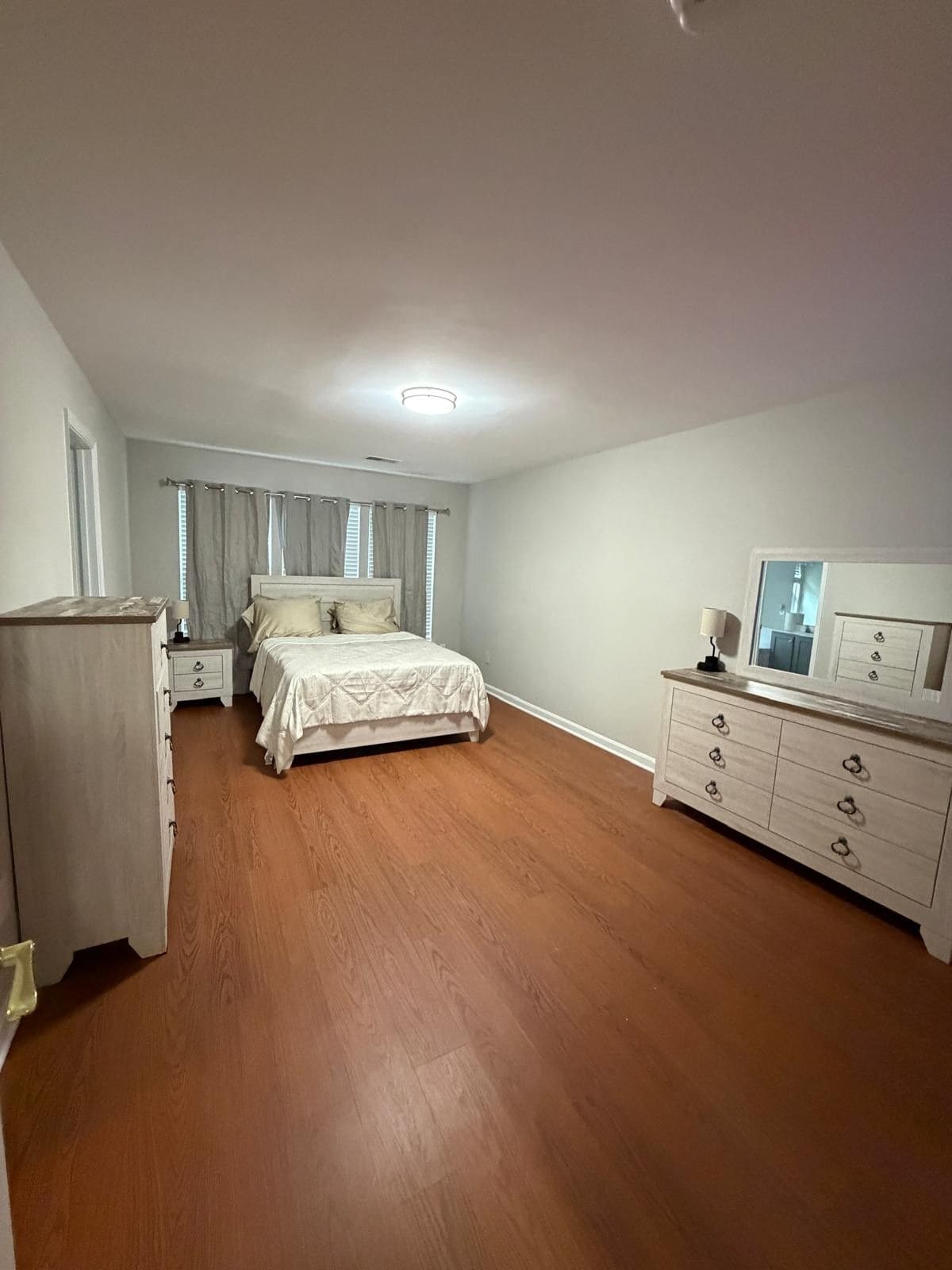 A bedroom with a bed, a dresser, a nightstand, and a mirror.