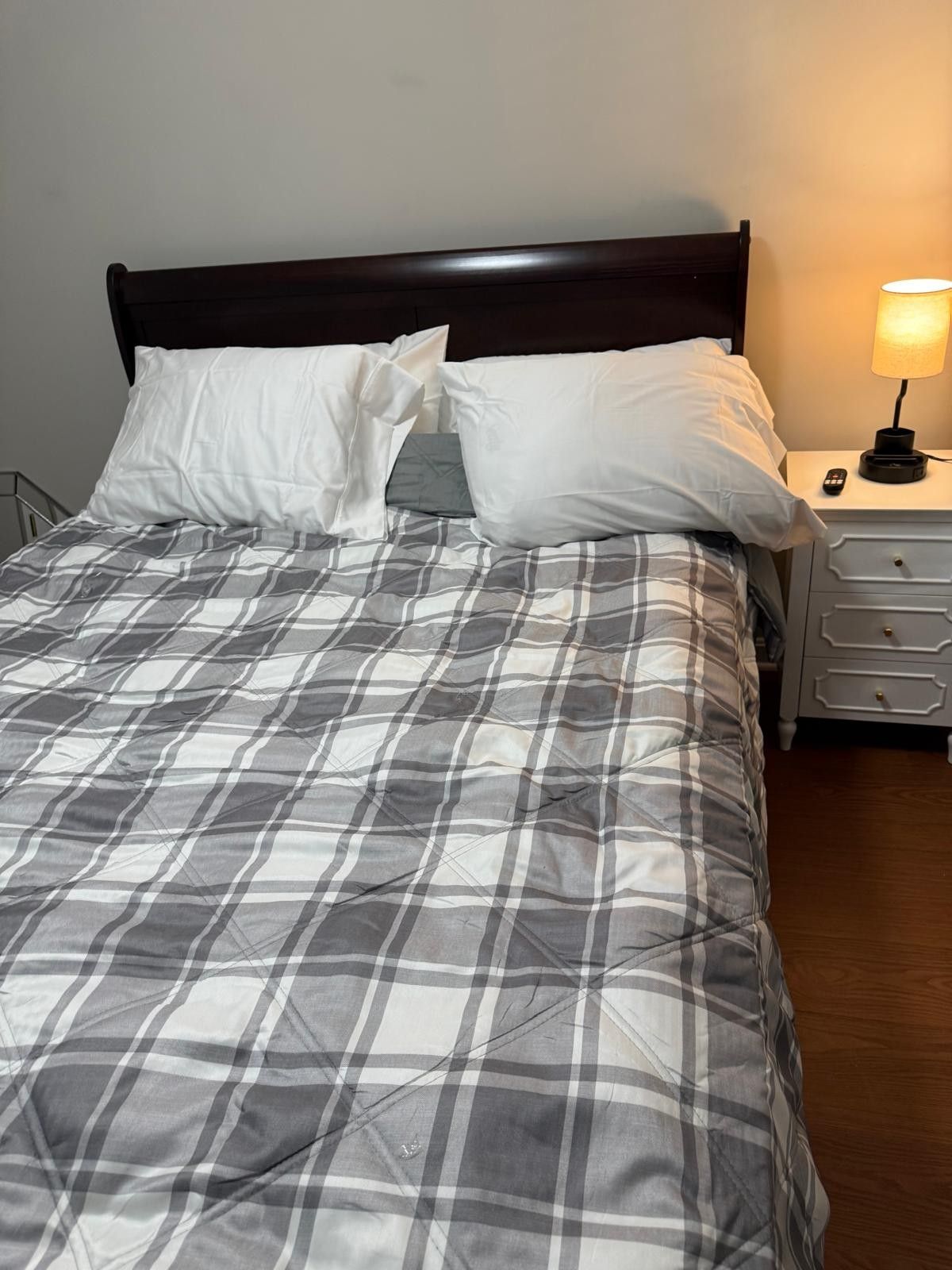 A neatly made bed with a plaid bedspread, white pillows, and a wooden headboard.