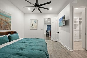 Une chambre à coucher avec un lit, un ventilateur de plafond, un tableau accroché au mur et un téléviseur fixé au mur.