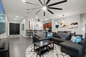 A modern living room with a sectional sofa, a coffee table, and a ceiling fan. - 4BR Heated Pool w BBQ in Central Area (Pinellas Park)