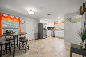 A modern kitchen with a dining area, featuring a refrigerator, stove, sink, and a clock on the wall. - 3BR Screened Heated Saltwater Pool • BBQ (Port Richey)