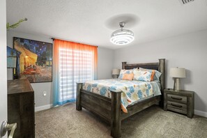 Une chambre à coucher avec un lit, deux tables de chevet, une lampe, un luminaire au plafond, une fenêtre avec des rideaux et un tableau au mur.