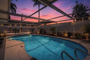 Une piscine intérieure avec vue sur le coucher de soleil, entourée de plantes et dotée d’un espace couvert avec des garde-corps.