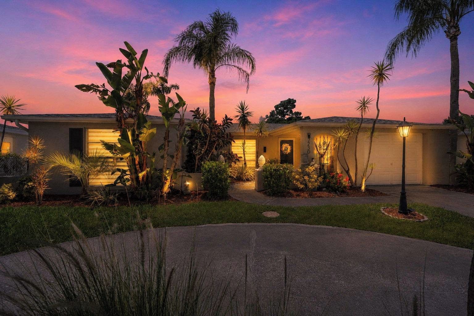 A residential property with a driveway, palm trees, and a well-lit entrance.