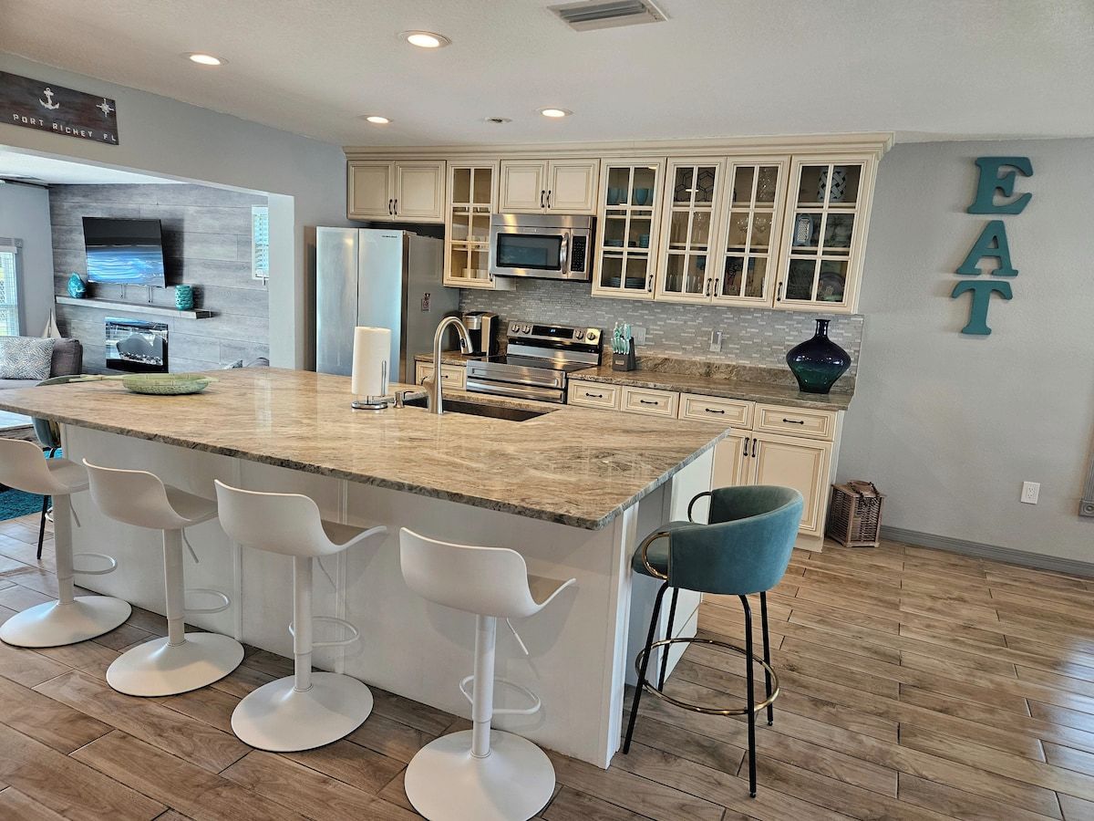 A modern kitchen with a central island, bar stools, and a dining area.