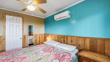 Ein Schlafzimmer mit einem hölzernen Kopfteil, einem Bett mit farbenfroher, gemusterter Bettdecke, einem Deckenventilator und einer Klimaanlage.