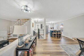 A spacious living area with a staircase, a dining area with wooden chairs, and a kitchen in the background. - Family Friendly Cottage on Lake Lanier (Dawsonville)