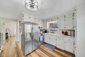 A modern kitchen with white cabinetry, a stainless steel refrigerator, a built-in oven, and a window providing natural light. - Family Friendly Cottage on Lake Lanier (Dawsonville)