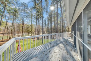 Une terrasse en bois avec une balustrade blanche donnant sur une pelouse et des arbres.