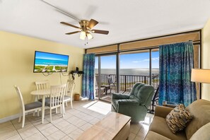 A room with a balcony, a ceiling fan, a television, and a dining area. - BraveWave 1BR King Bed Bay Views Pool & Pier at Laguna Reef (Rockport)