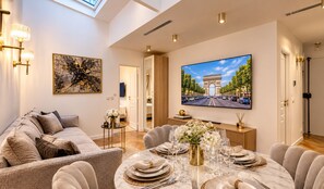 Ein modernes Wohnzimmer mit einer Couch, einem Esstisch für sechs Personen, einem Flachbildfernseher und Kunstwerken an den Wänden.