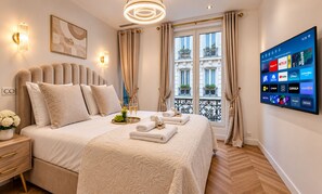 Ein Hotelzimmer mit einem großen Bett, einem Flachbildfernseher, der Streaming-Dienste anzeigt, und einem Balkon mit Blumentöpfen.