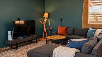 Uma sala de estar com televisão, sofá, mesa de centro e abajur.