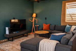 Uma sala de estar com televisão, sofá, mesa de centro e abajur.