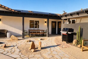 Eine Außenpatio mit Steinboden, einem Grill und einem Essbereich mit Stühlen und einem Tisch.