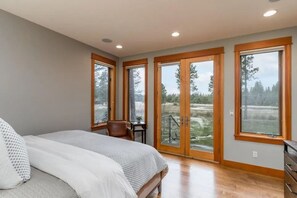 Ein Schlafzimmer mit Bett, Stuhl, Schreibtisch und großem Fenster mit Blick auf eine natürliche Landschaft.