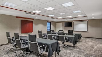 A conference room with a carpeted floor, multiple tables with chairs, a projector screen, and a door.