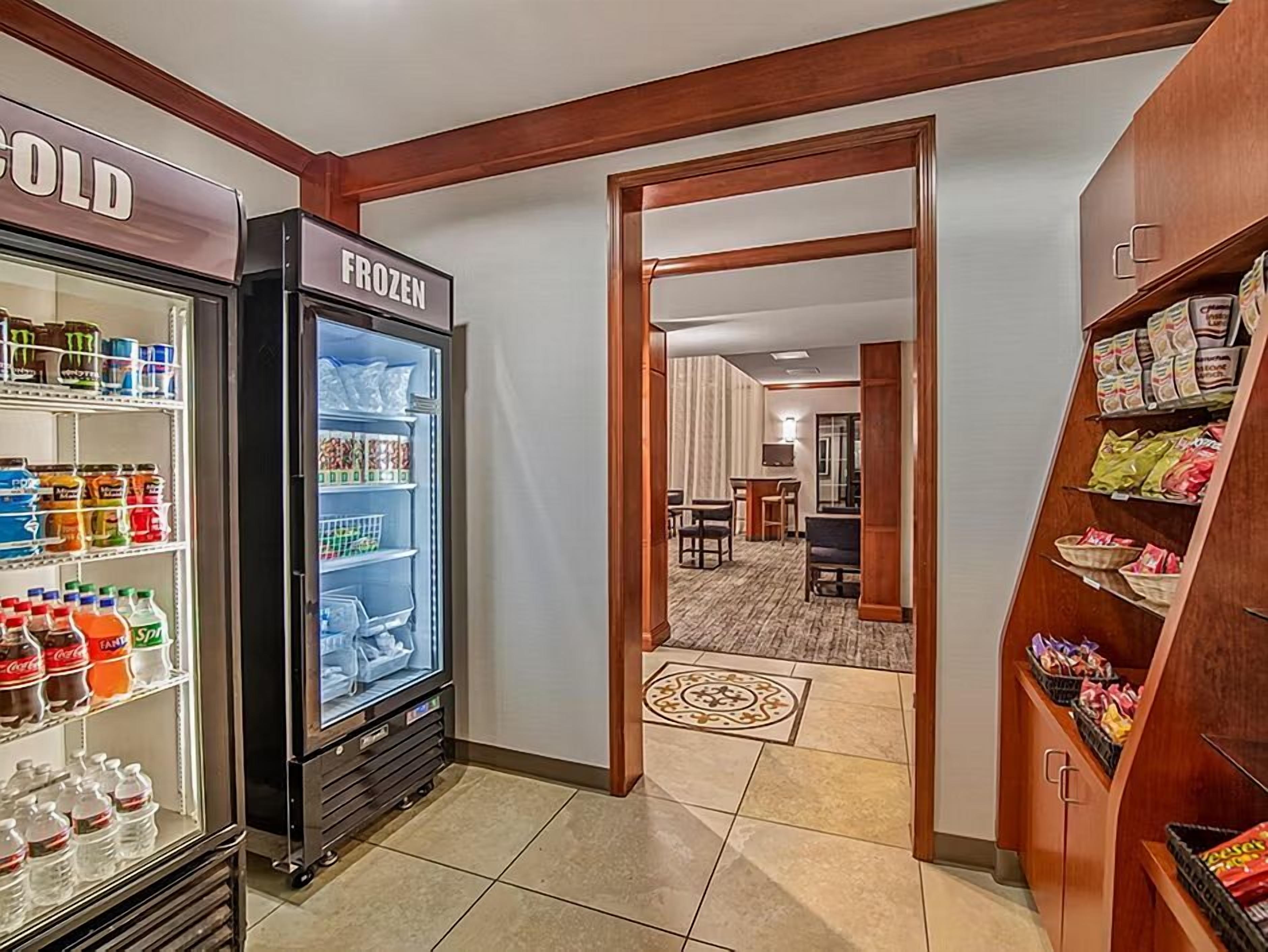 A hotel lobby with a refrigerated display case labeled 'COLD' and 'FROZEN,' a carpeted area leading to a dining room, and a snack shelf.