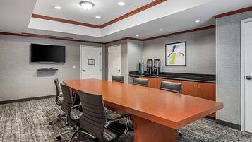 A conference room with a long table, chairs, a flat-screen TV, and a coffee station.