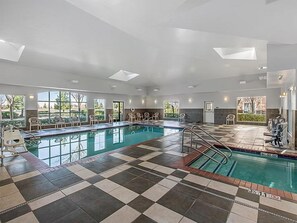 Una amplia piscina interior con suelo a cuadros, varias ventanas y un techo iluminado por el sol.