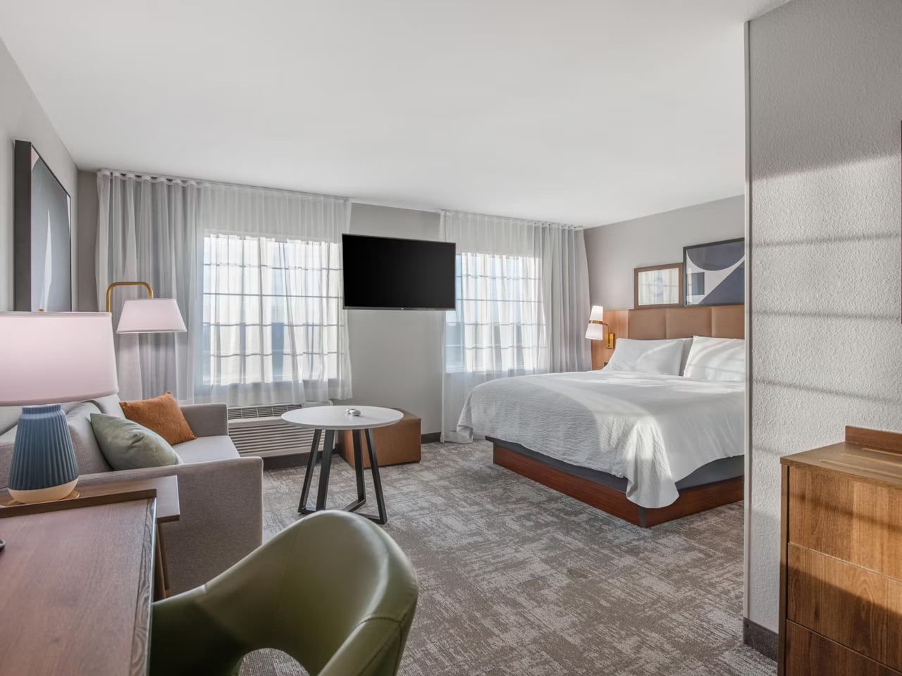 A hotel room with a bed, a desk, a chair, a TV, and a window with curtains.
