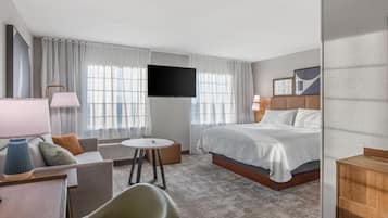 A hotel room with a bed, a desk, a chair, a TV, and a window with curtains.